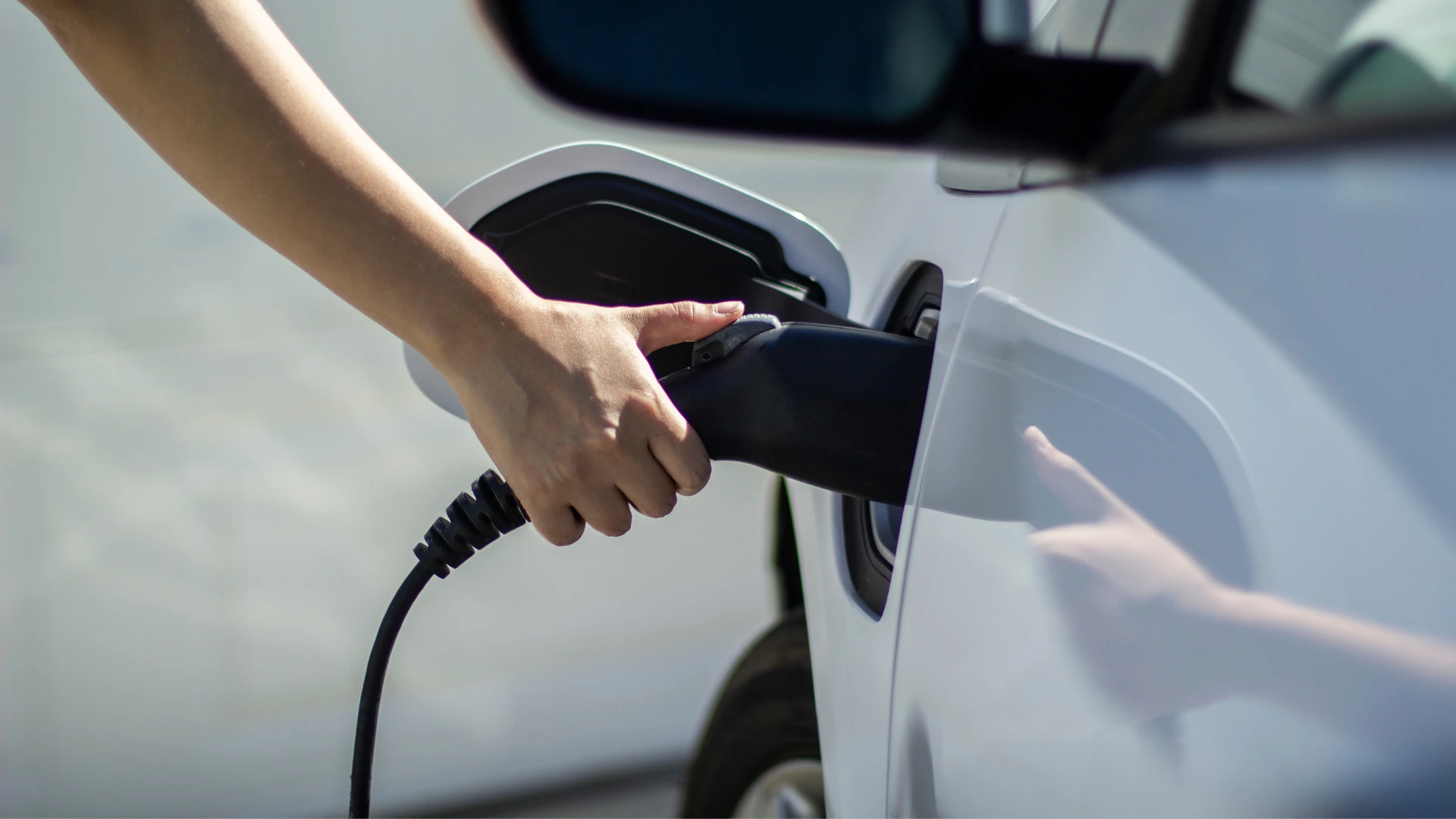 una chica carga un coche eléctrico mientras mira un móvil